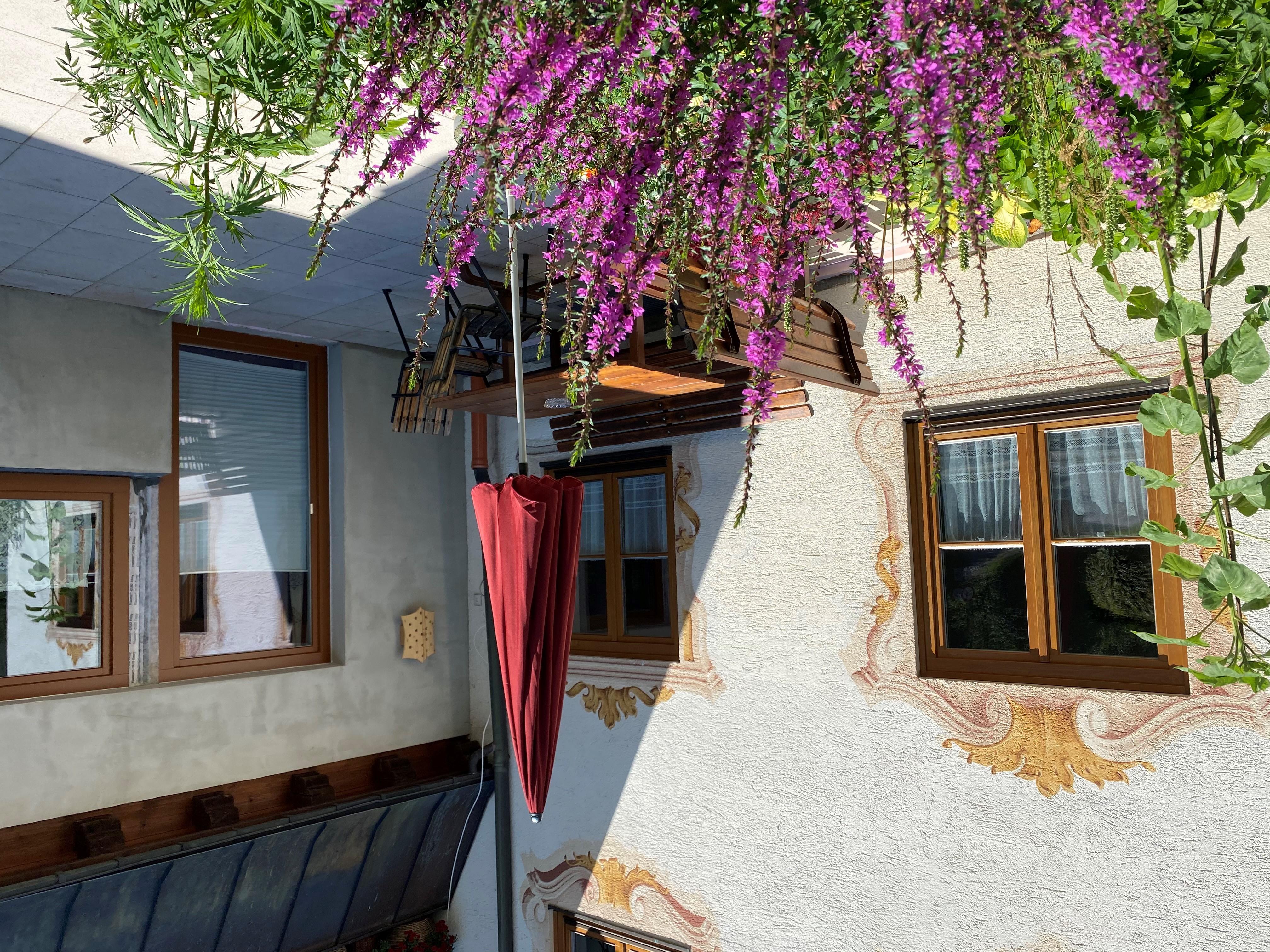 A cozy outdoor area with a table and chairs, surrounded by colorful flowers. The sunshade provides pleasant shade on a sunny day.