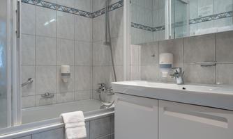 A modern bathroom with a shower and bathtub. The walls are light tiled, and there is an elegant sink cabinet.