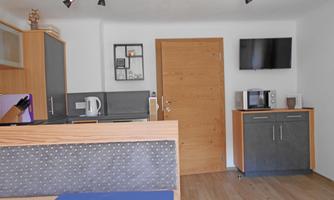 A modern and bright kitchen unit with a wooden shelf and a television. The furniture is arranged in a functional and stylish manner.