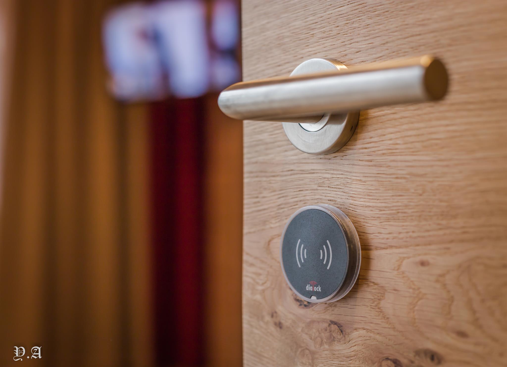 A metal door handle and a digital access symbol on a wooden door. The background is blurred and shows a room.