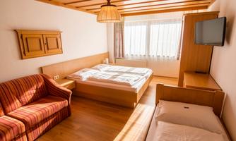 A cozy bedroom with a double bed, a sturdy sofa, and an additional bed. Large windows provide plenty of daylight and a warm atmosphere.