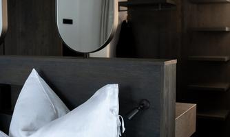 A modern bedroom with a large bed and white pillows. On the wall, there are mirrors and shelves in dark wood.