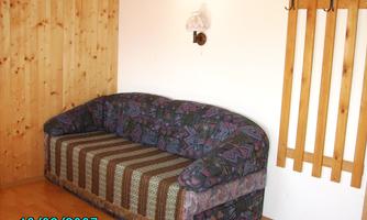A cozy sofa with a colorful pattern is situated in a simply furnished room. Wooden panels and a coat rack are mounted on the wall.