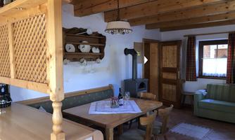 A cozy dining area with wooden decor and a rustic table. In the background, a seating area and a kitchen are visible.