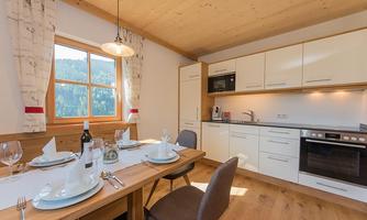 A modern kitchen with a wooden dining area and a view of the mountains. The table is set for dinner, with dishes and glassware.