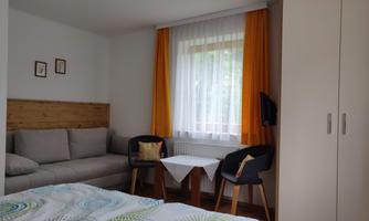 A cozy room with a bright sofa and colorful curtains. A small table and a wardrobe complete the furnishings.