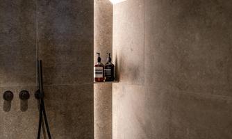 A modern shower with gray tiles and soft lighting. Care products are ready on a shelf.