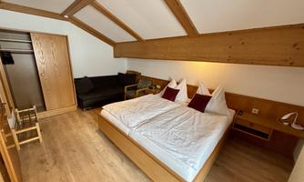 A cozy room with a double bed and two pillows. The wooden elements and the bright floor create a warm atmosphere.