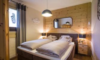 A cozy bedroom with wood paneling and a large bed. The room is well-lit and has elegant nightstands.