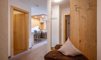 A modern entrance area with wooden details and a cozy seating area. In the background, an open living and dining room is visible.