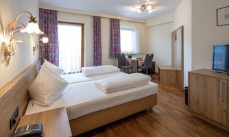 A modern hotel room with two single beds and a wooden floor. There are windows with curtains and a TV in the room.
