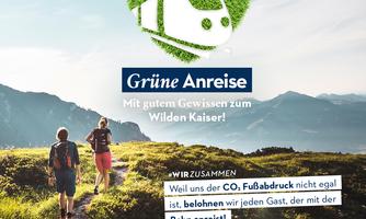 A pair of hikers enjoys the view in the mountains. The focus is on eco-friendly travel by train to the Wilder Kaiser.