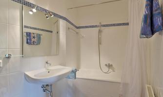 A modern bathroom with a bathtub and a shower. The walls are tiled white, and a mirror reflects the light.