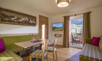 A cozy living space with wooden floors and modern furniture. Large windows offer a view of nature.