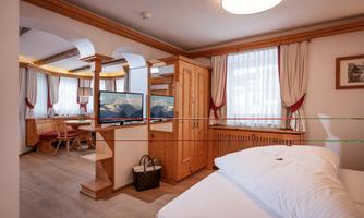 A cozy hotel room with wooden paneling and a large window. The room features a bed, television, and a small workspace.