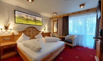A cozy room with a large double bed and a warm wood look. The window offers a view of a balcony with plenty of daylight.