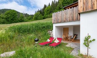 A cozy terrace with red loungers and a small grill. In the background, green meadows and forests can be seen.