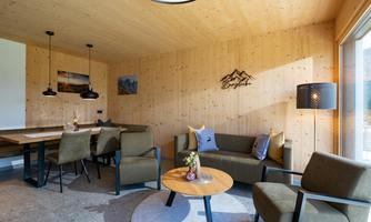 A cozy living space with wood-paneled walls. There is a sitting area, a dining table, and large windows that let in plenty of light.