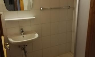 A simple bathroom with a shower, sink, and wall mirror. The walls are tiled in neutral colors.