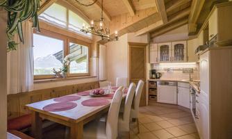 A bright kitchen with wooden details and a large table. Large windows provide a view of the surrounding landscape.