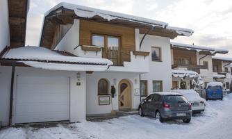 A modern house in the snow with a large garage door and a car in front of it. The sky is cloudy and there is a layer of fresh snow on the ground.