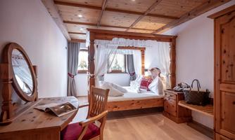 A cozy bedroom with a wooden four-poster bed and soft curtains. The room is bright and cheerful, featuring a desk and a mirror.