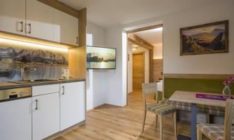 A modern kitchen with wooden details and a small dining area. The walls are light, and a picture with a landscape motif hangs on the wall.