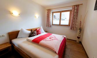 A cozy bedroom with a large bed and decorative pillows. The room has a window with curtains and warm light.