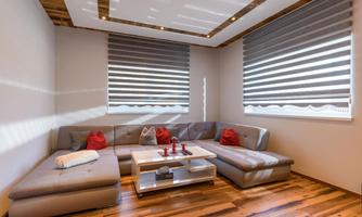 A modern living room with a gray sofa and red pillows. The wooden floor and the blinds create a cozy atmosphere.