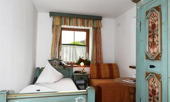 A cozy room with a single bed and a traditionally wood-carved wardrobe. The window lets in a lot of light, and the walls are painted in soft colors.