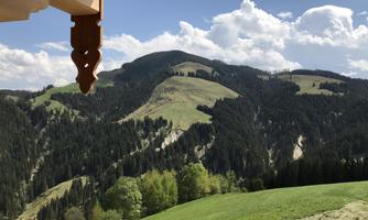 A beautiful mountain landscape with green meadows and wooded slopes. The sky is blue with some clouds.