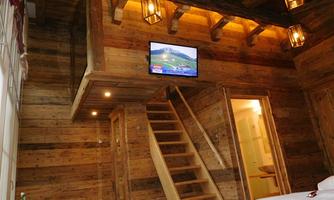 A cozy room with wood paneling and warm light. A staircase leads to another area, while a television hangs on the wall.