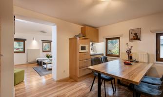 A cozy dining area with a wooden table and modern chairs. In the background, the kitchen and a living area are visible.