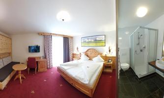 A cozy hotel room with a double bed, a small table, and a seating area. On the right side is a modern bathroom with a shower and sink.