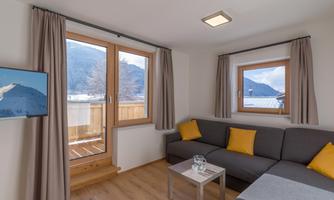 A bright living room with a gray sofa and yellow cushions. Large windows offer a view of the mountains.