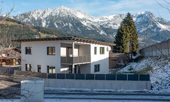 A modern house in the mountains, surrounded by snow-covered landscapes. In the background, impressive mountains lie under a clear sky.