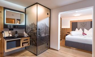 A modern hotel room with a separate area for the bathroom. The room features a large bed and comfortable wooden furniture.