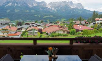 A beautiful view from a balcony of a picturesque landscape with mountains in the background. The lower houses are surrounded by green meadows, and the atmosphere feels peaceful.