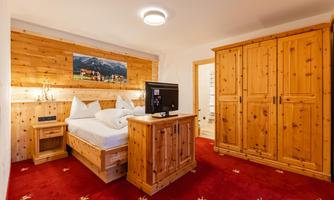 A cozy room with wood paneling and red carpets. There is a comfortable bed, a TV, and a wardrobe.