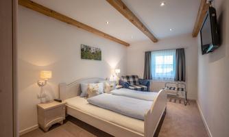 A cozy bedroom with two beds, a television, and an armchair. Soft lighting and bright colors create an inviting atmosphere.