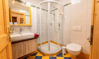 A modernly designed bathroom with a shower and a sink. The floor is tiled with colorful tiles in yellow and blue.