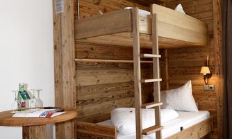 A bright room with a wooden bunk bed and a small table. The floor is made of wood, and the walls are also made of natural untreated wood.