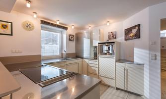 A modern kitchen with bright furniture and gray surfaces. Large windows provide plenty of daylight.