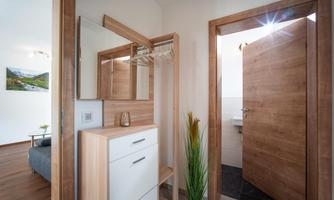 A modern hallway with wooden cabinets and mirrors. The door leads to a bathroom, while a stylish decorative element is visible in the background.