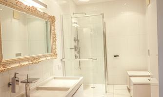 A modern bathroom with a glass shower and an elegant mirror. The walls are kept in bright white, and there is a stylish sink shelf.