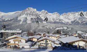 A picturesque winter landscape with snow-covered mountains and charming cabins. A cable car glides over the snowy surroundings.