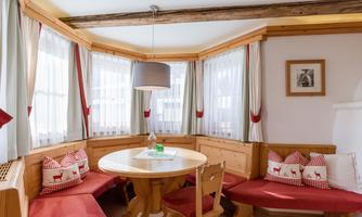 A cozy dining area with wooden-paneled walls and a round table. The red cushions and large windows create a friendly atmosphere.