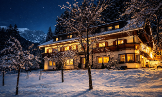A cozy house in the snow, illuminated by warm light. The night sky is clear and dotted with stars.