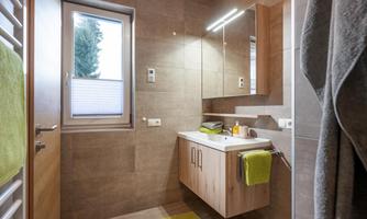 A modern bathroom with wooden cabinets and bright tiles. There is a large window and green towels that add accents.