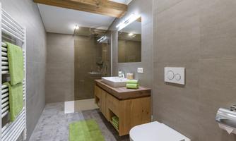 A modern bathroom with wooden details and bright tiles. It features a shower, a sink, and green towels.
